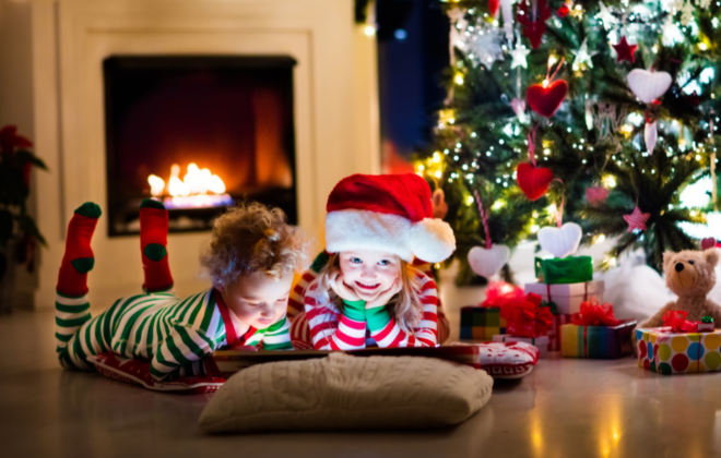 Children reading a book with a Christmas tree in the background.